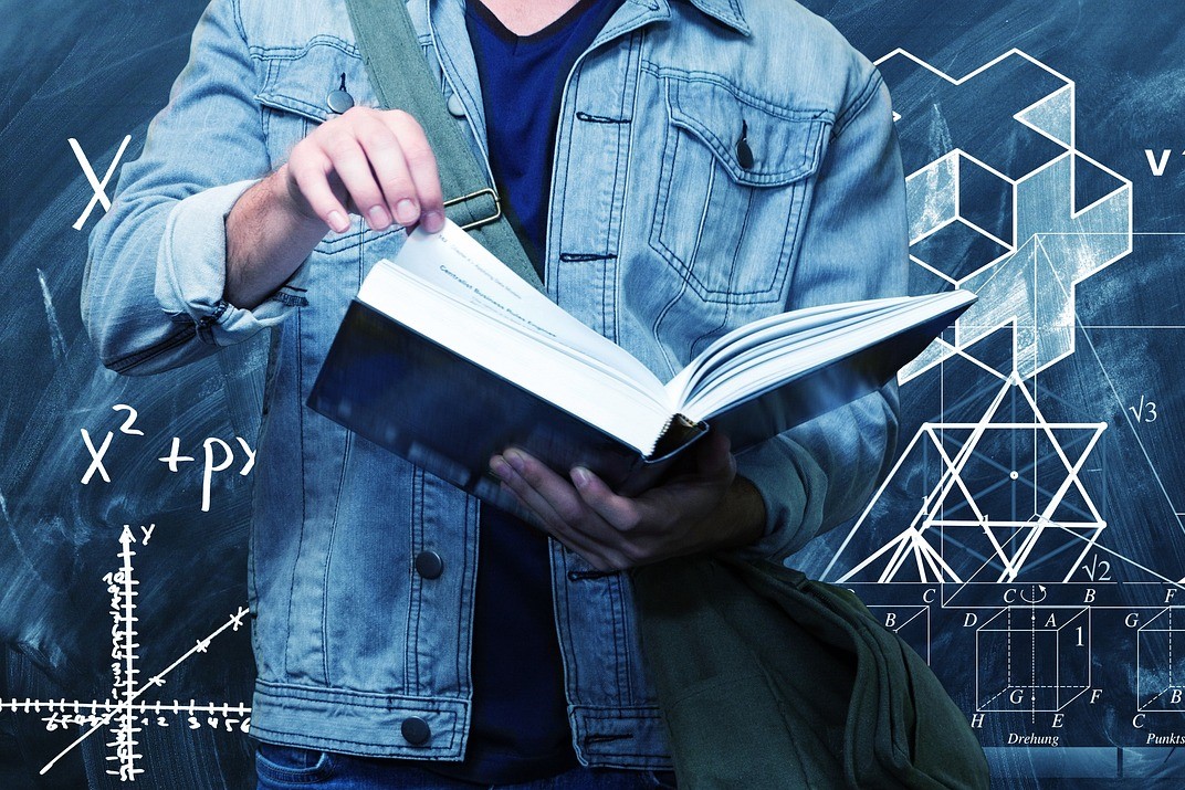 Człowiek trzymający książkę, za nim wykresy i wzory matematyczne